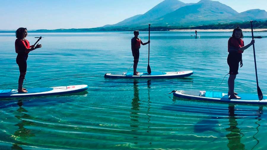 Three girls SUPing on the sea with mountains in the background