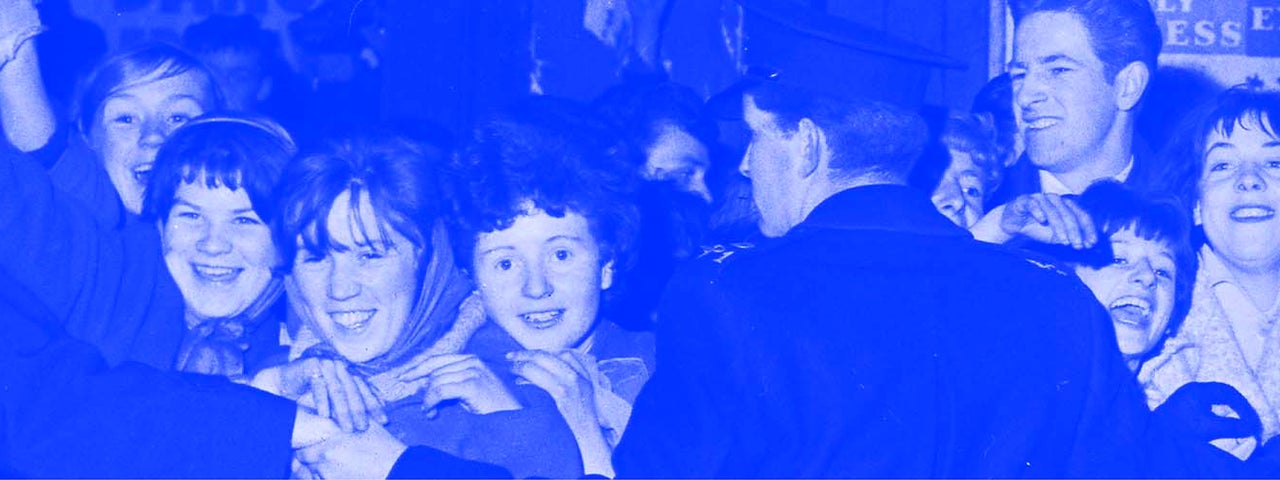 Blue and grey photo from 60s of happy young women waiting for an idol being held back by line of men