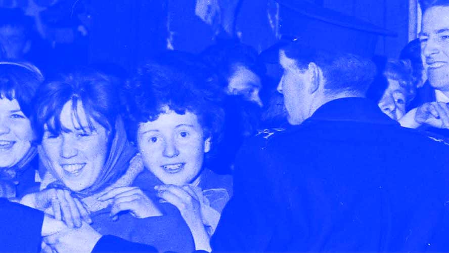 Blue and grey photo from 60s of happy young women waiting for an idol being held back by line of men