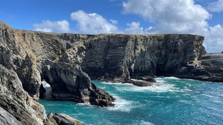 A view of cliffs and a sea arch under a blue sky