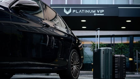 A black car parked outside a building with two upright suitcases placed beside it