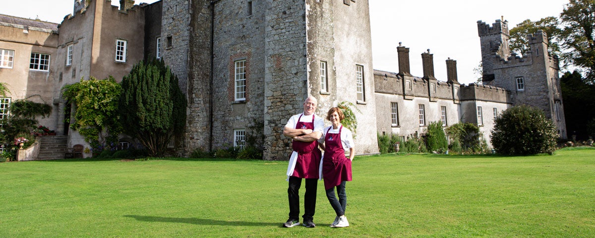 Two people in chef uniforms standing in front of a castle