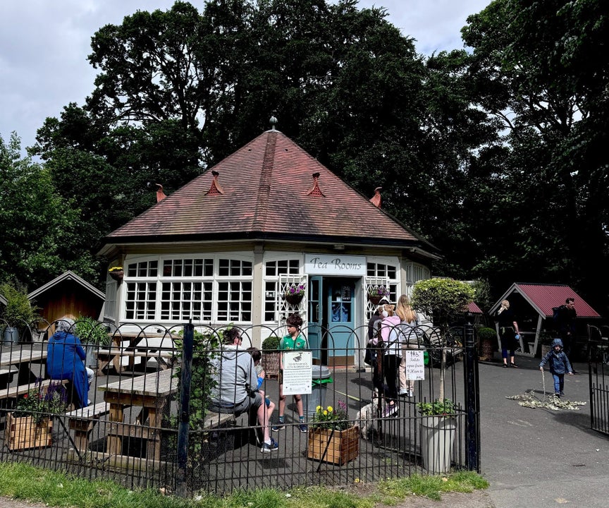 White circular building with a red roof with bench and people all behind black railings