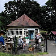 White circular building with a red roof with bench and people all behind black railings