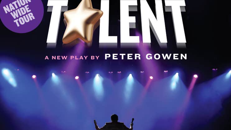 Viewed from the back of a stage, a figure is silhouetted against front of stage with spotlights shining down on it with large white event text above.