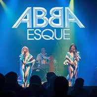 ABBAESQUE 2 women in colourful costumes on a stage singing.