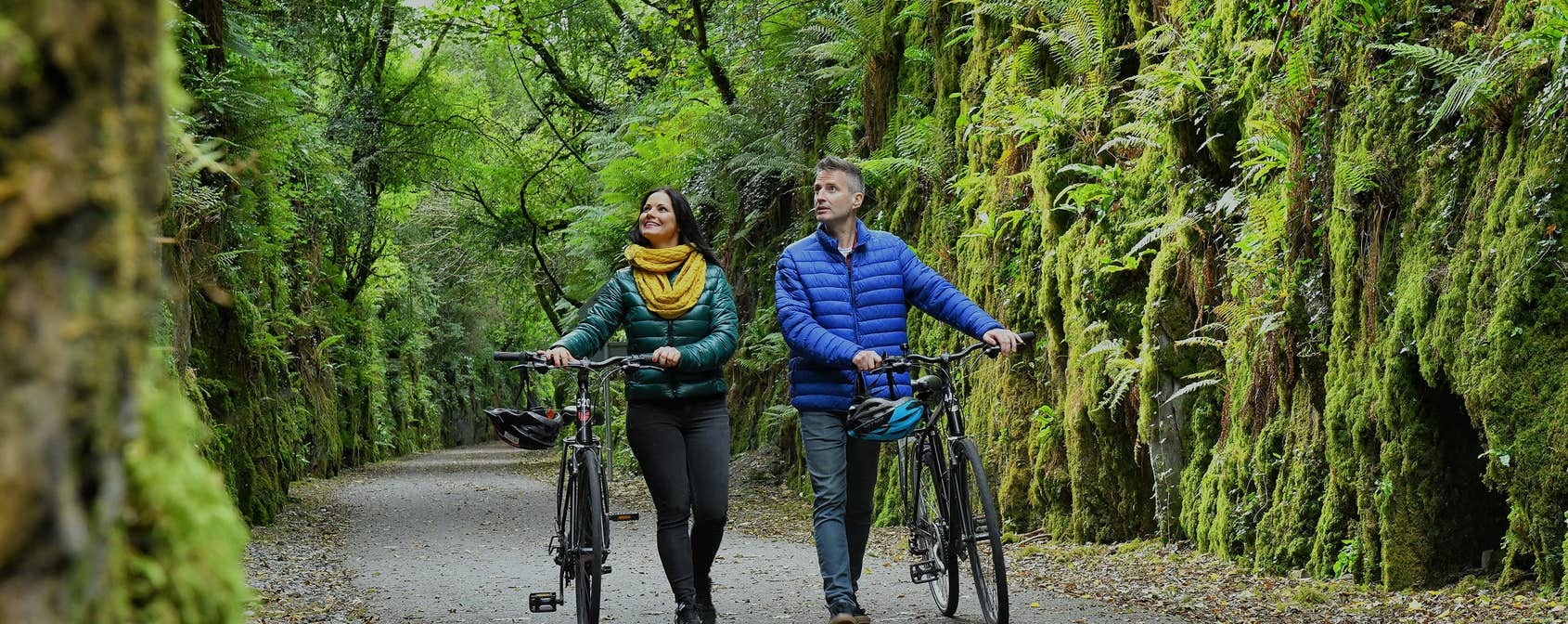 Man and woman walking their bikes through the Waterford Greenway 