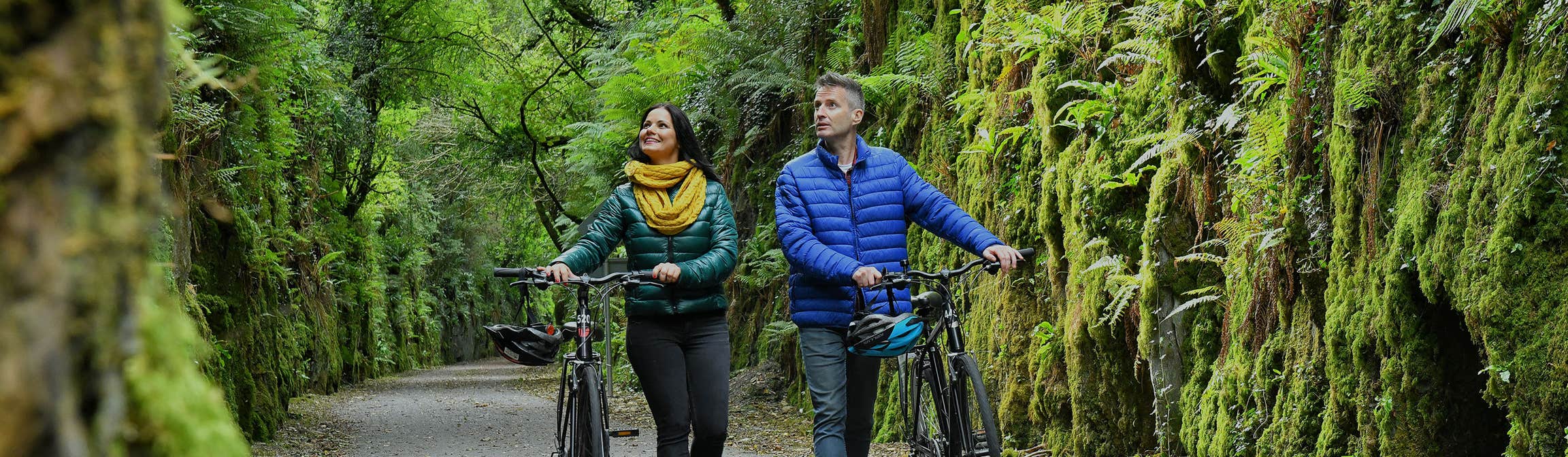Man and woman walking their bikes through the Waterford Greenway