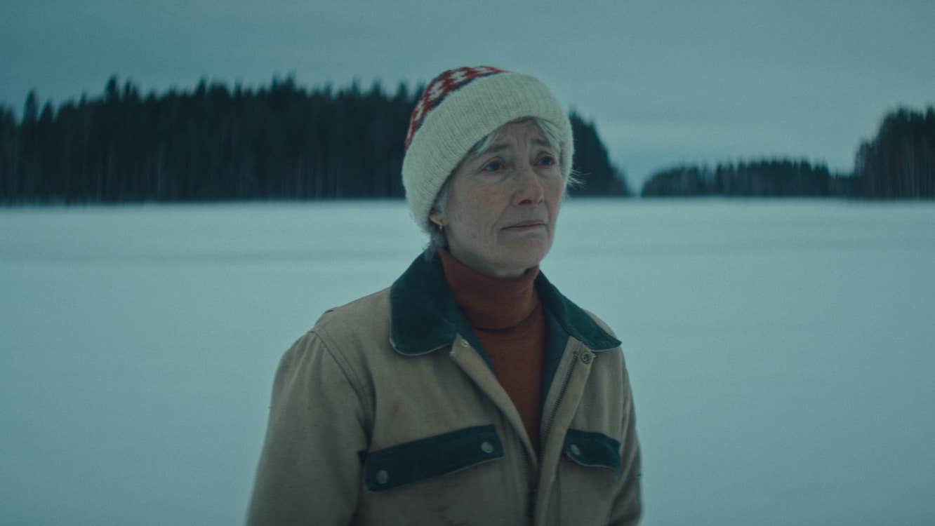 An old woman in warm clothes is in a snowy wilderness.