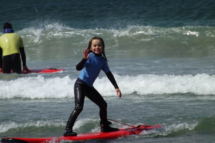 A young girl standing on a red surf board in the sea