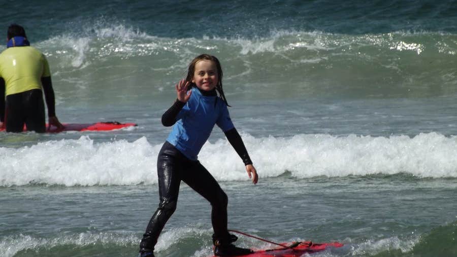 A young girl standing on a red surf board in the sea