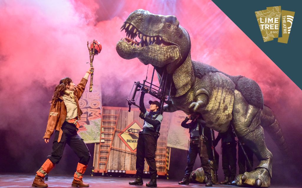 On a stage people are working a large animatronic puppet of a dinosaur, a person in a costume is holding something up to it on a stick