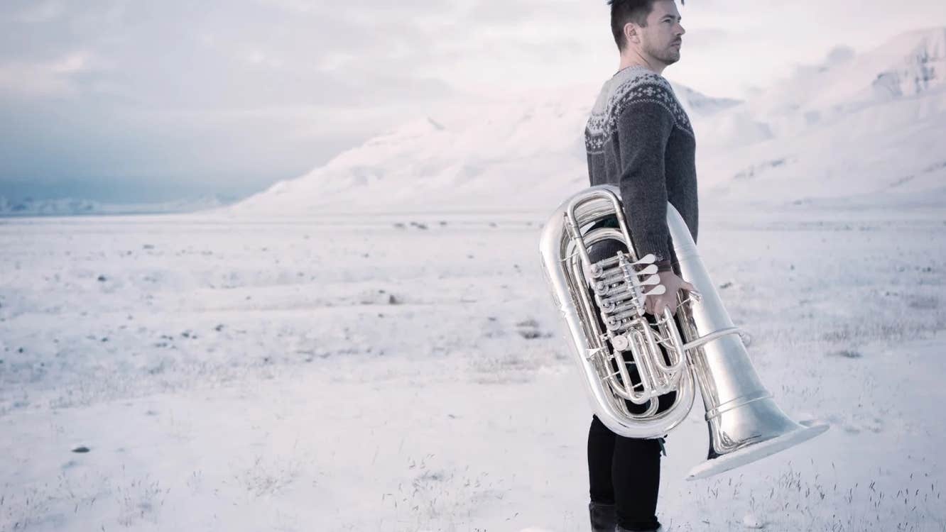 A man with a tuba is standing on a beach