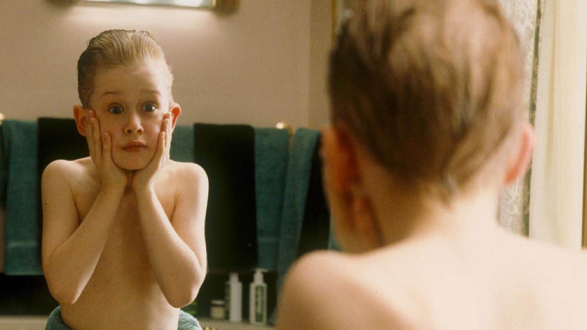 Reflection in mirror of young boy holding hands up to his face looking shocked.