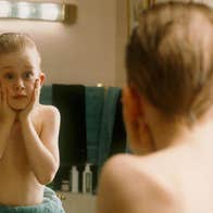 Reflection in mirror of young boy holding hands up to his face looking shocked.