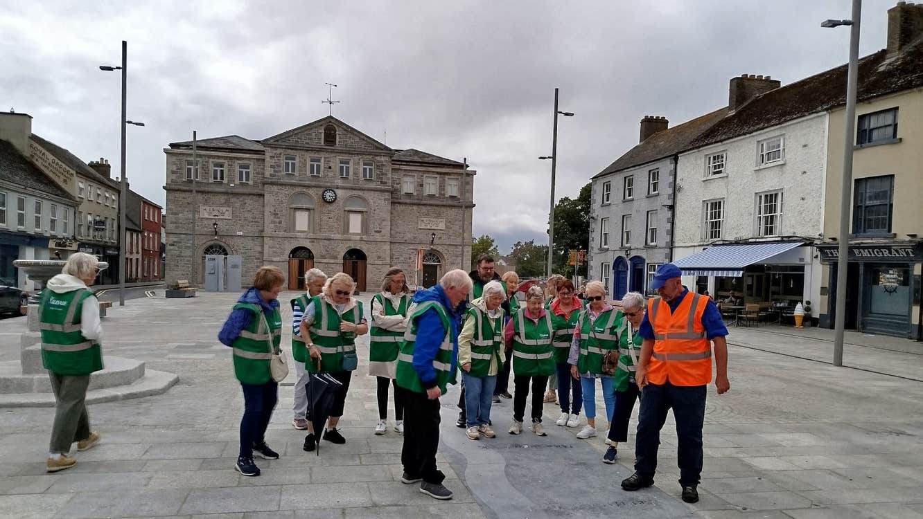 Group wearing green jackets led by a guide in an orange jacket all looking at the ground in Athy