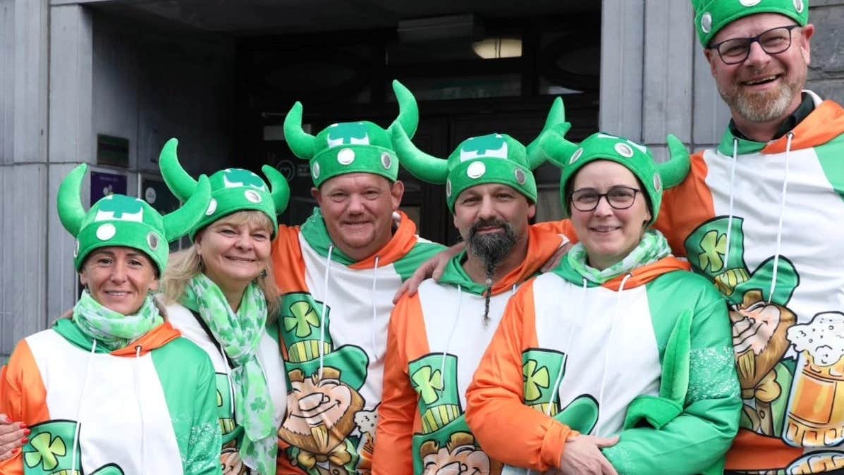 Group of smiling people in green hats with horns and sweatshirts with smiling leprechauns.