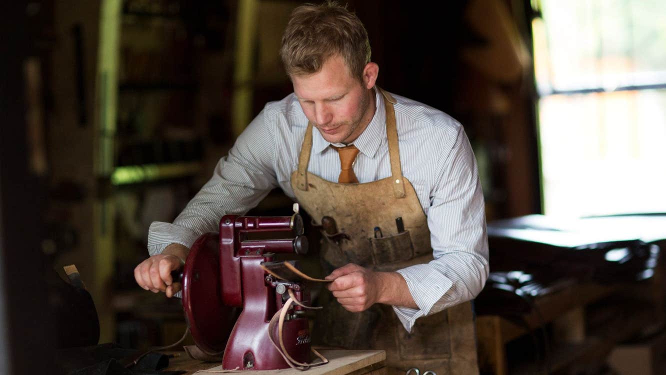 A craftsman in an apron working on a leather bag