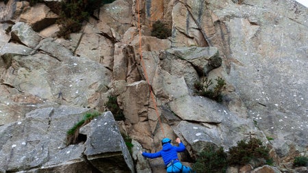 Person climbing while another person holds a rope on top of a rock
