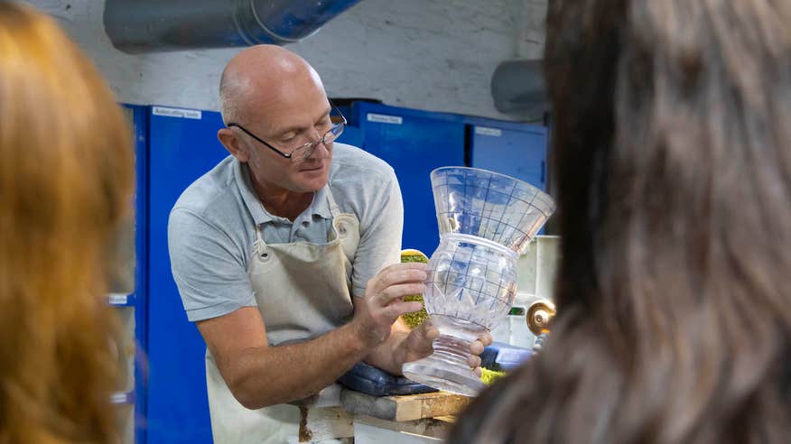 A craftsman in the House of Waterford Crystal in Waterford showcasing a piece of crystal to people.