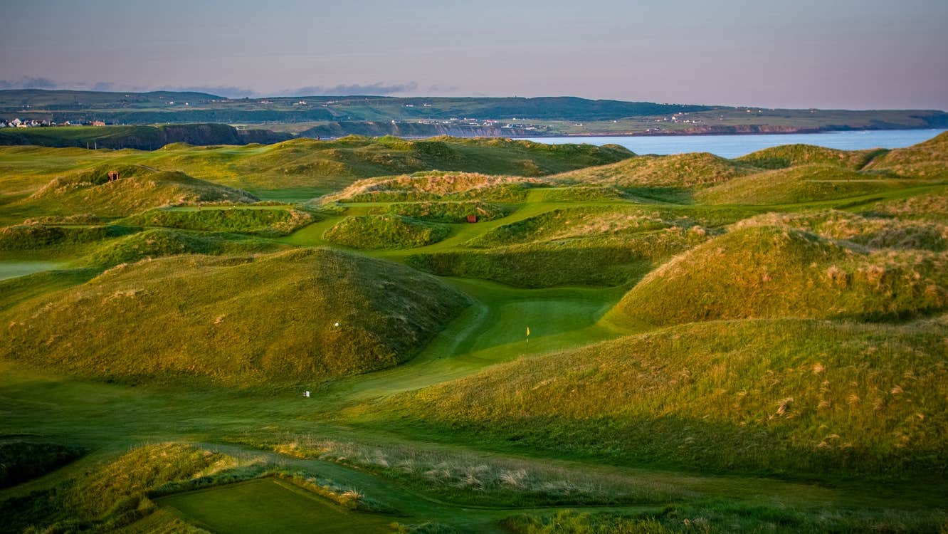 A golf course with grassy dunes and the coast in the distance