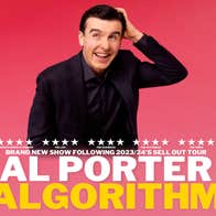 A laughing man in dark suit is scratching his head with left hand, against bright pink background.