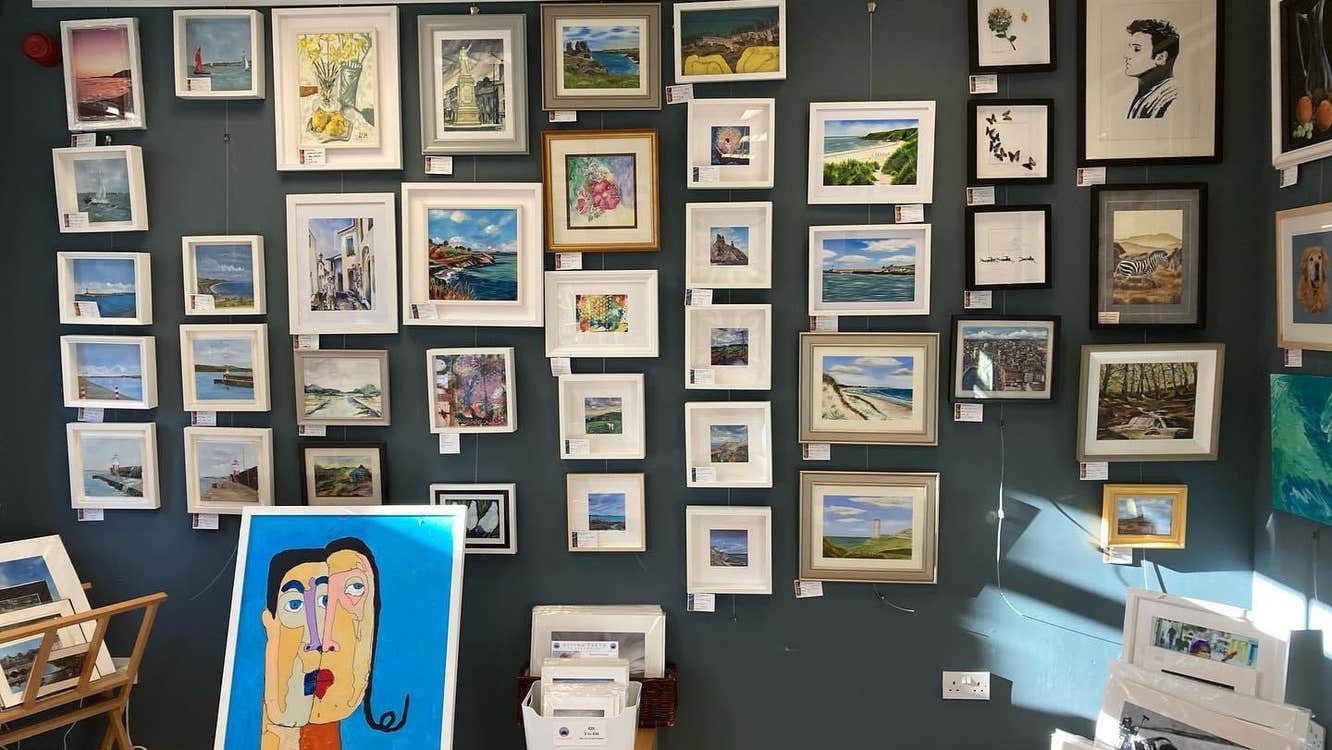 Teal wall with paintings displayed and a white box with prints in front of it