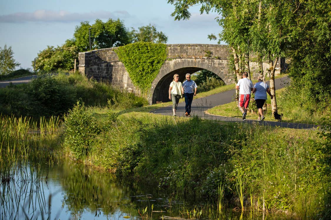 Two couples walk past each other on the Royal Canal Greenway near a stone bridge