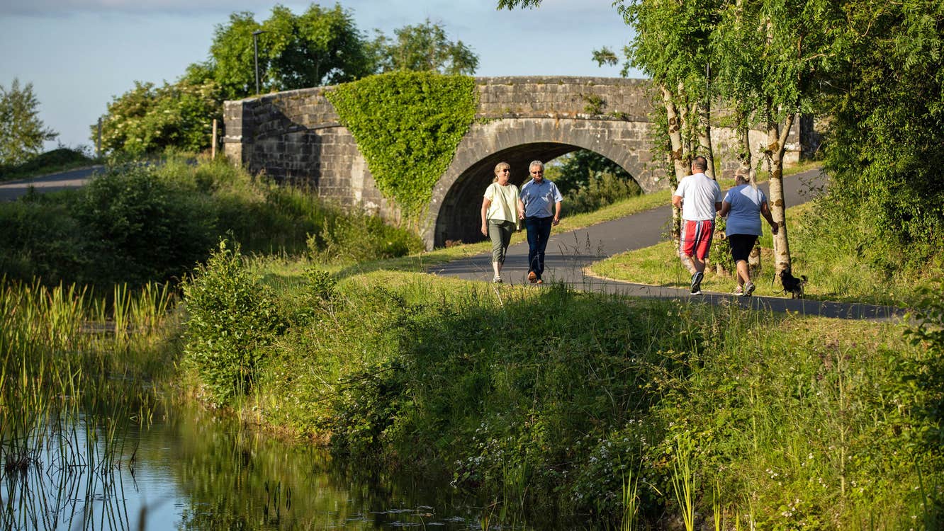 Two couples walk past each other on the Royal Canal Greenway near a stone bridge