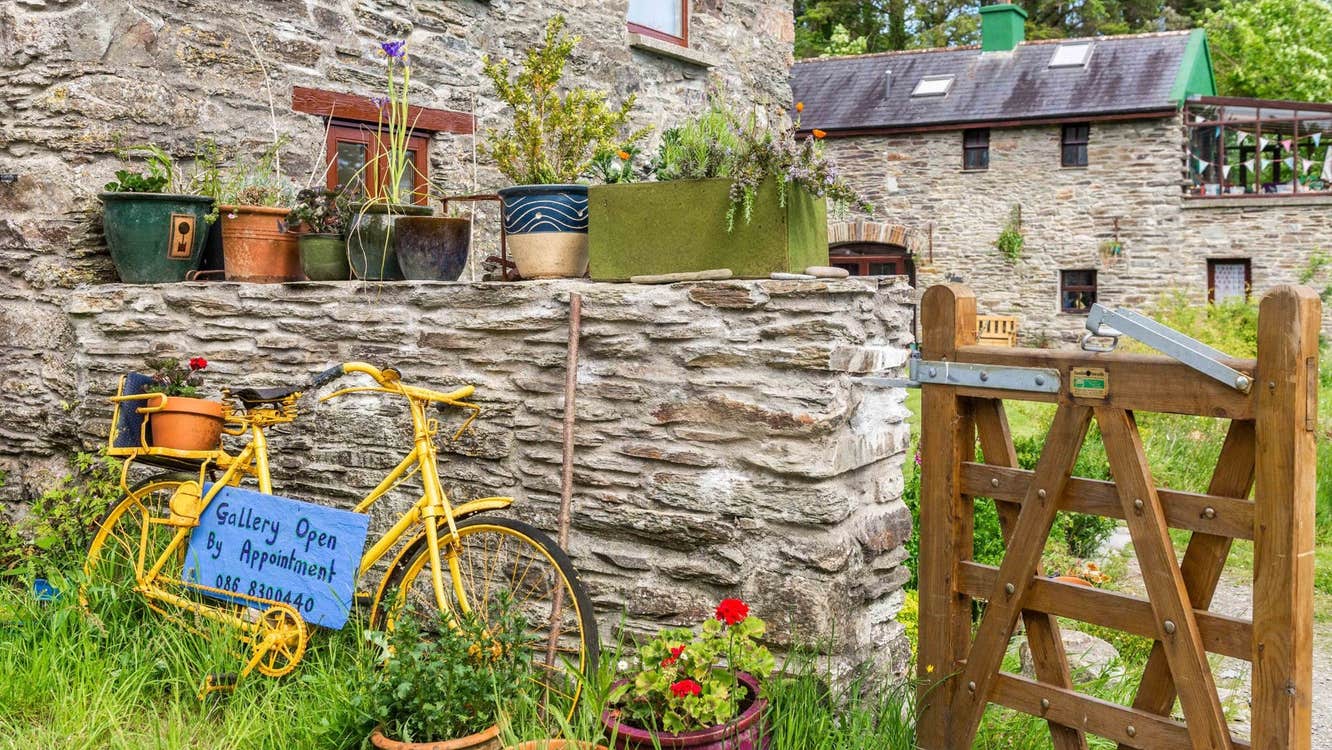 Stone house and wall with a yellow bike resting against it a wooden gate and pots of flowers