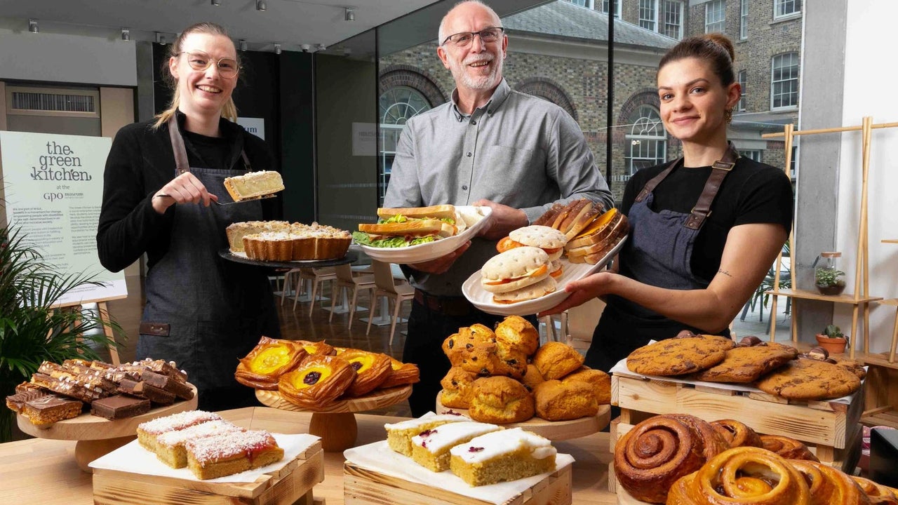 Three people holding food with a display of pastries on a counter in front of them