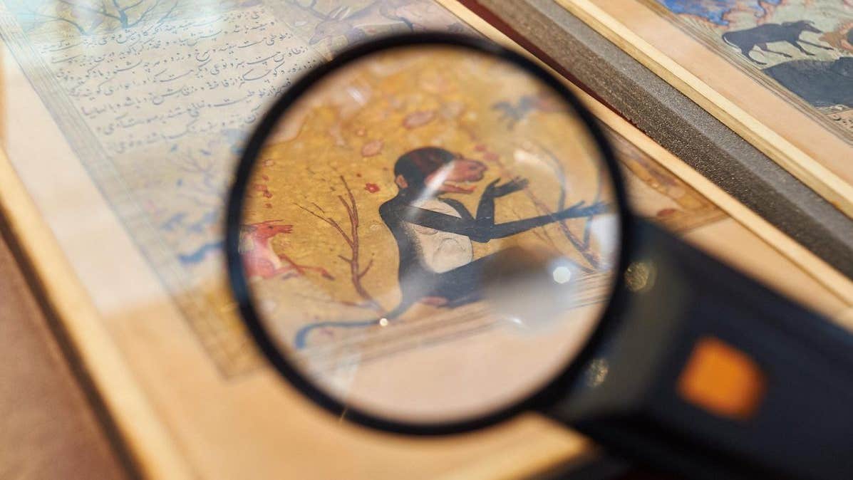 Close up view seen via a black magnifier of an old drawing of a monkey in a book.