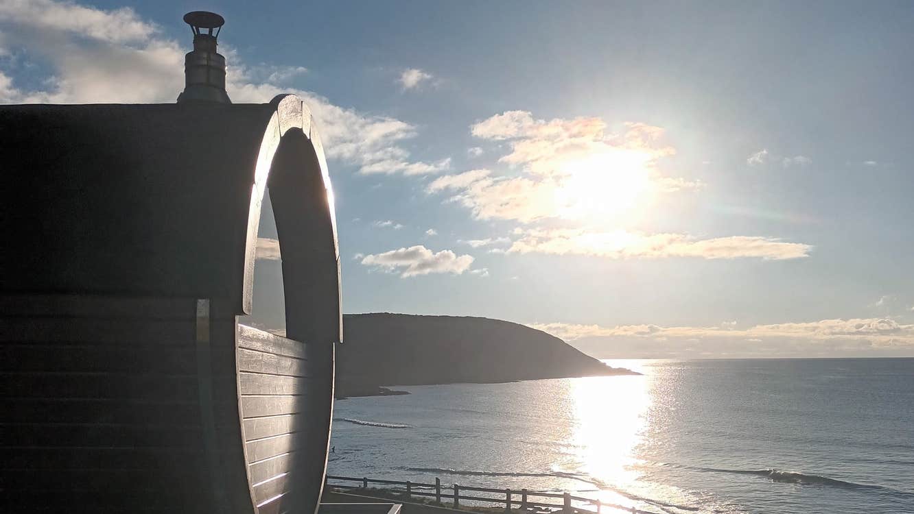Mobile sauna by a beach with the sun setting over the sea