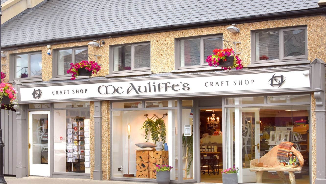 Grey yellow and white shop front with two hanging baskets and two flower pots at the entrance