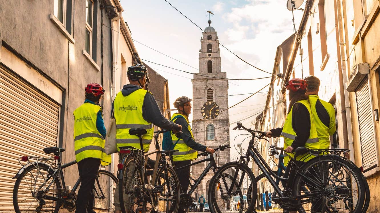 Group of people with bikes and hi vis vests standing facing a clock tower