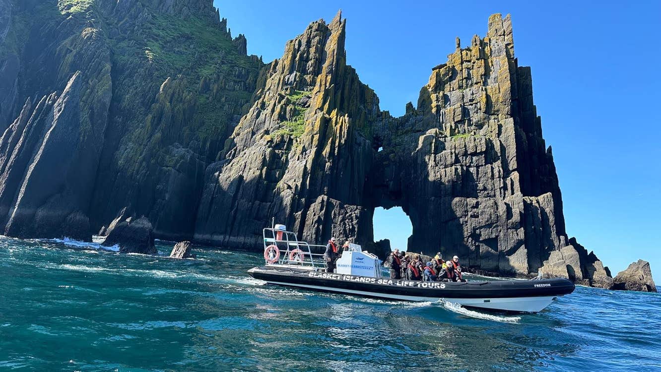 A group of people in a boat in front of a sea arch