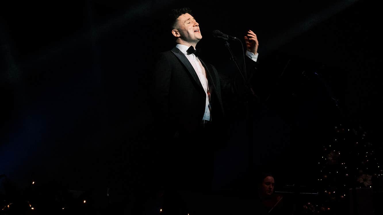 Eamonn Walsh in a suit, singing in a black void.