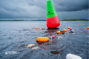 On a large body of water, there is a large upright red and green buoy with a line of smaller floatss.