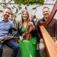 Trad musicians Mairéad Ní Mhaonaigh, Mark Redmond & Cormac De Barra, sitting on a wall together with their instruments