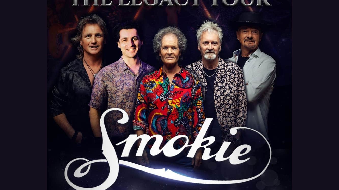 A group of 5 gently smiling men, some wearing patterned shirts, against black background.