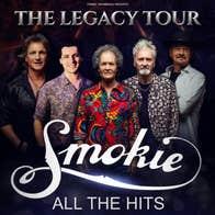 A group of 5 gently smiling men, some wearing patterned shirts, against black background.