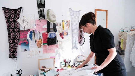 Artist working with materials on a desk with fabrics hanging on the wall