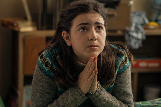 A girl is praying with hands together, looking upwards.