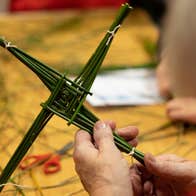A close of up view of pair of hands holding a green 4 pronged cross