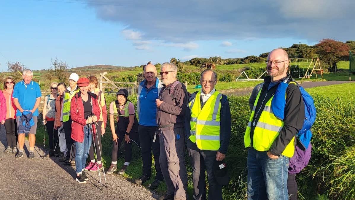 A group photo of people gathered by the edge of a country road, some wearing Hi Vis jackets.