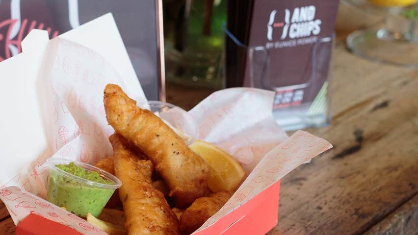 A portion of fish and chips in a box with a lemon slice and dip
