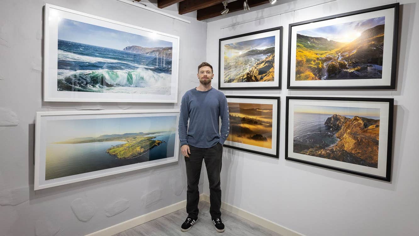 A wall with six large framed photographs and a man standing in front of them