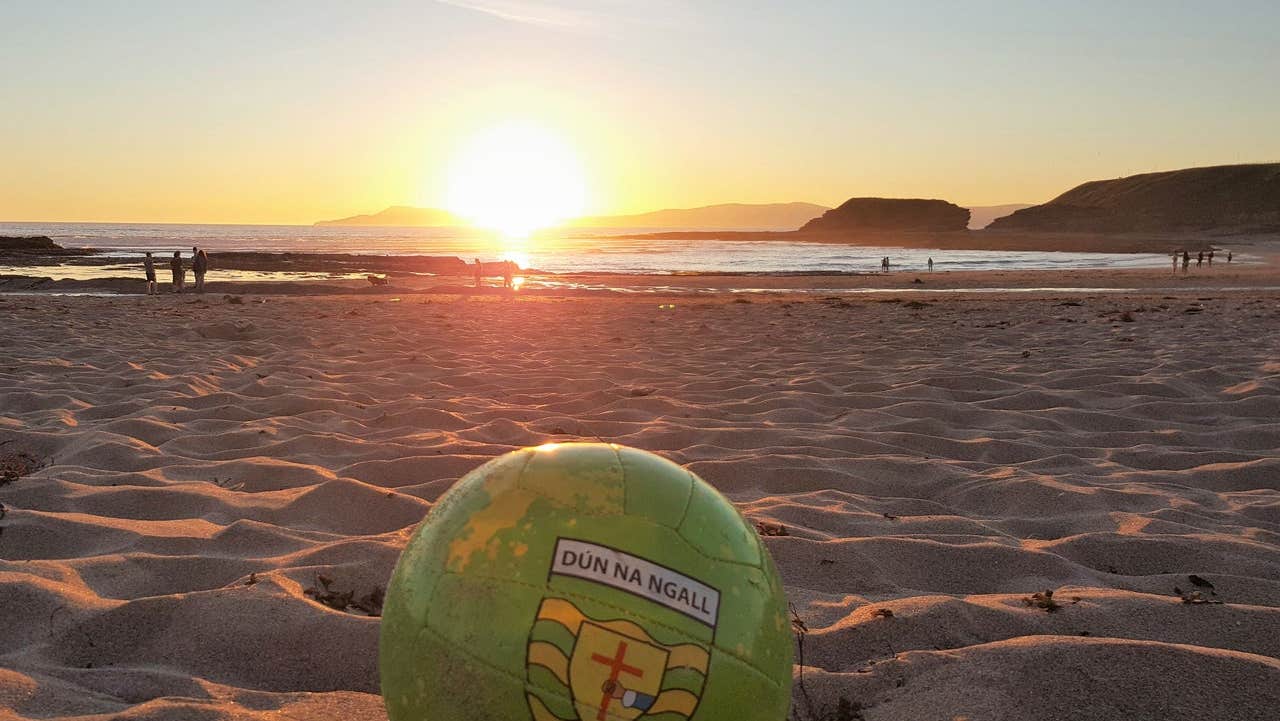 A view of a football sitting on a sandy beach at sunset