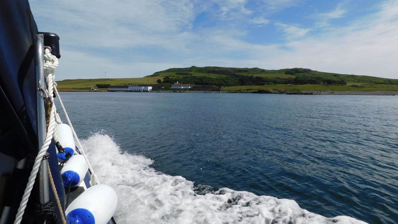 View from the side of a rib style boat travelling across the sea towards an island