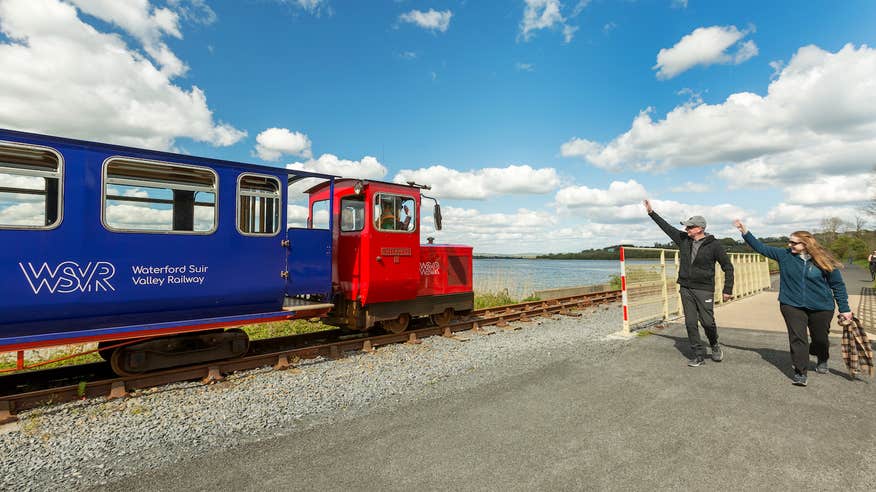 Two people waving at the Waterford Suir Valley Railway train as it goes by in County Waterford.